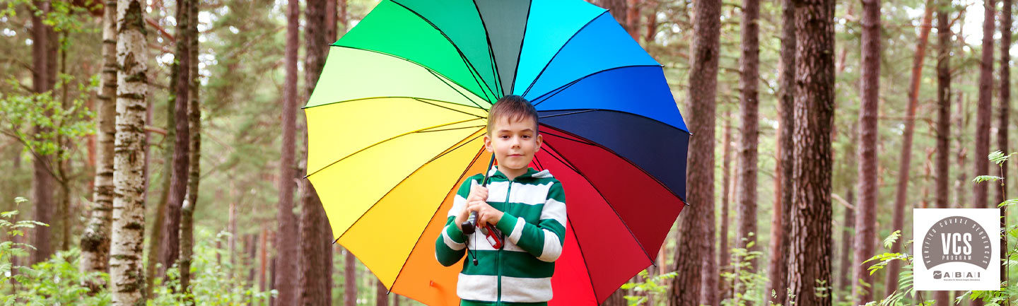 Portrait of young boy in the woods holding a rainbow umbrella