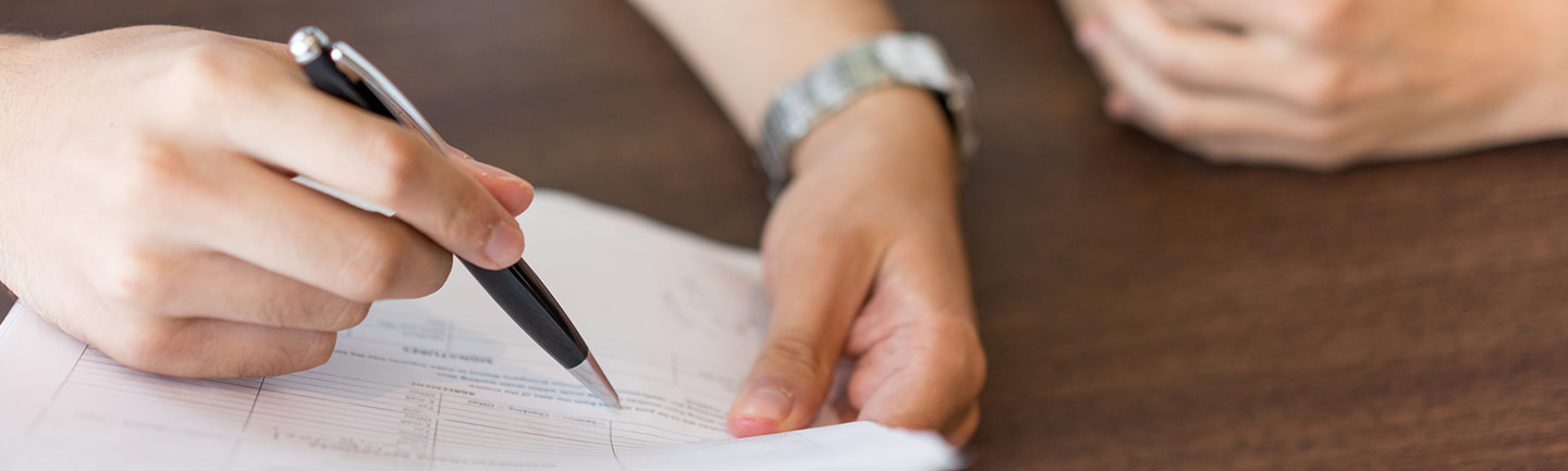 Photo of a hand holding a pen and looking over a chart on paper
