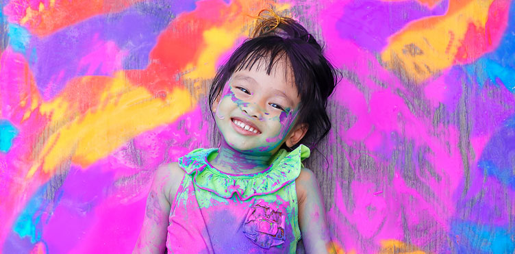 A young girl with colourful paint all around her and all over her