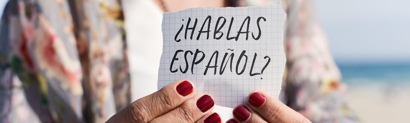 Person holding a piece of paper that says "hablos espanol?"