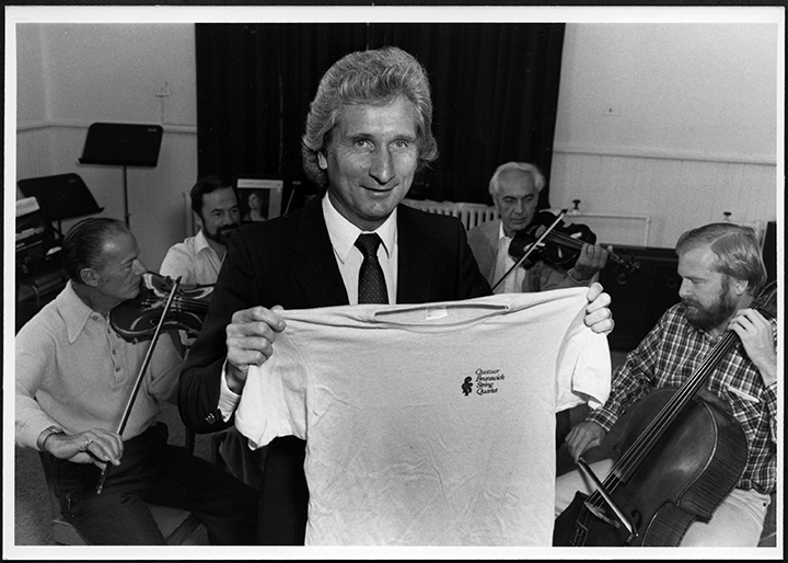 UNB president James Downey displays the t-shirt with logo for Brunswick String Quartet, 1983. Courtesy of UNB Archives, PR, File 767, no 9