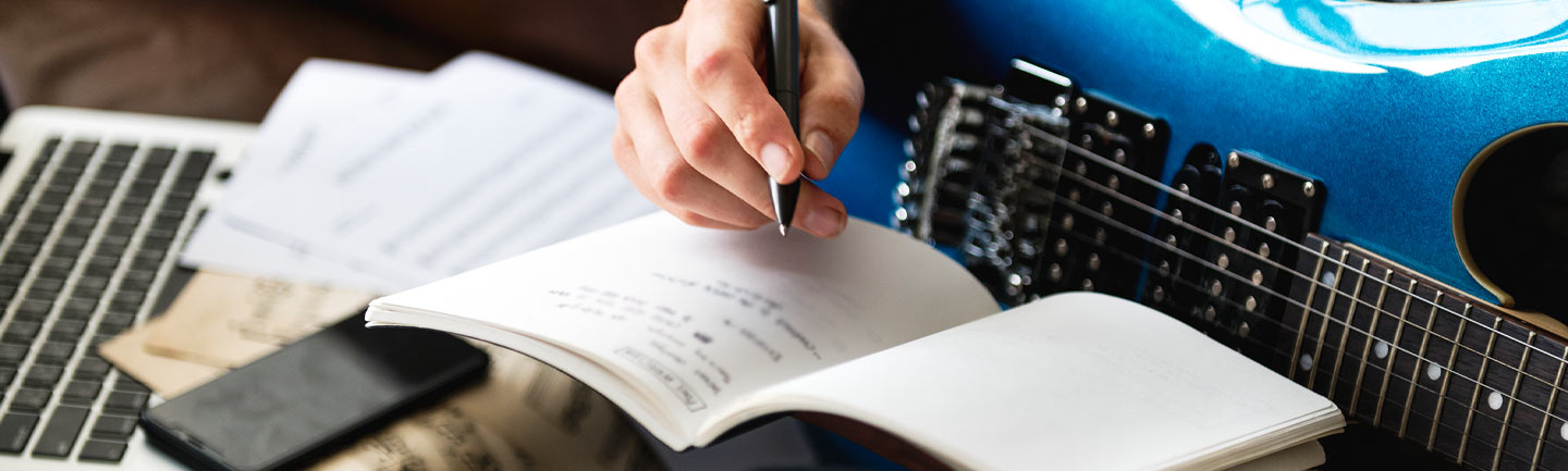 Photo of a person holding a guitar and writing in a notebook
