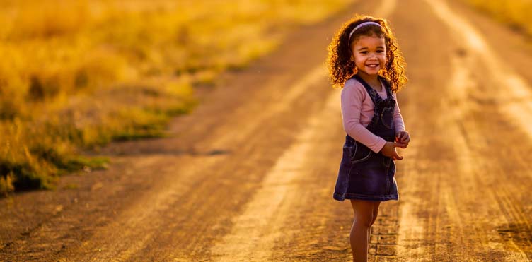 A child stands on a roadway looking back towards the viewer