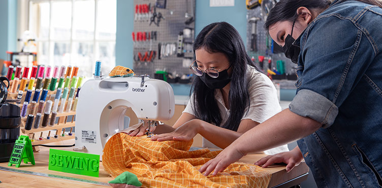 Two students work on sewing some colourful fabric