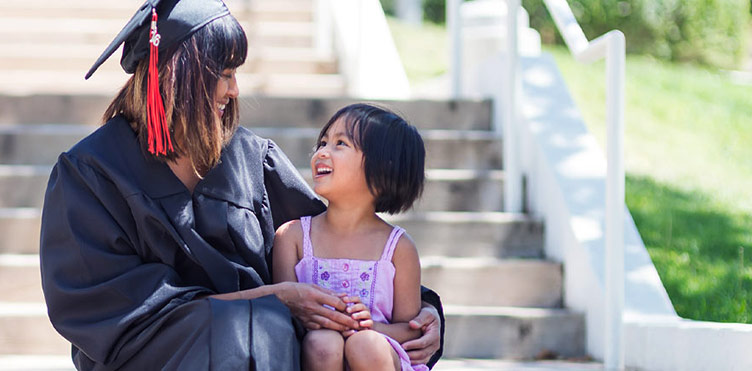 UNB Graduate with a small child sitting on steps outside.