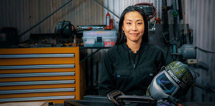 Skilled welder stands in front of a tool chest in an industrial workspace.