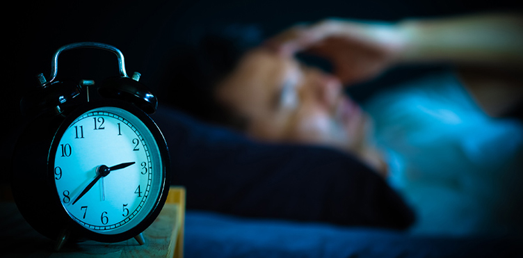 Analog clock showing 2:40 a.m. with a tired, frustrated individual in the background.