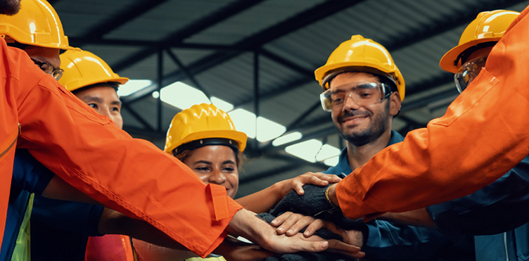 A group of workers in protective gear gather for a team huddle.