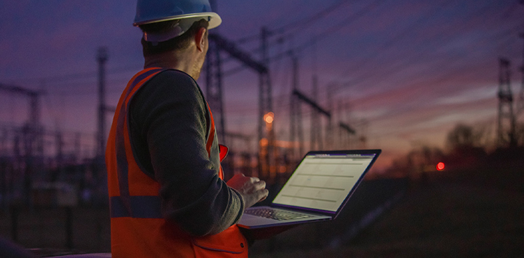 A worker checks power lines on-site using a laptop.