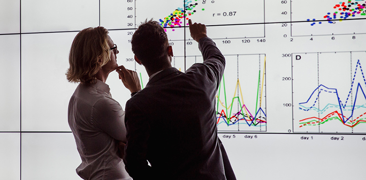 Photo of two professionals looking at a digital screen that has several charts on it