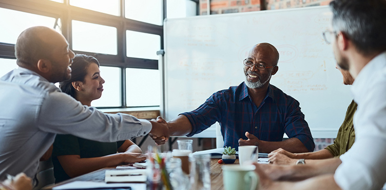Photo of multiple professionals in a meeting and two of them are shaking hands
