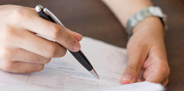 Photograph of a person writing on a piece of paper with a pen.