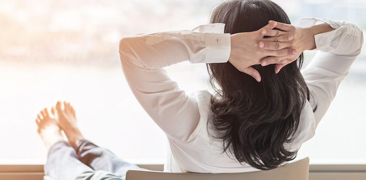 Photo of professional leaning back in a chair with her hands behind her head in a relaxed pose