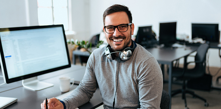Photo of a smiling man sitting at a desk with a computer