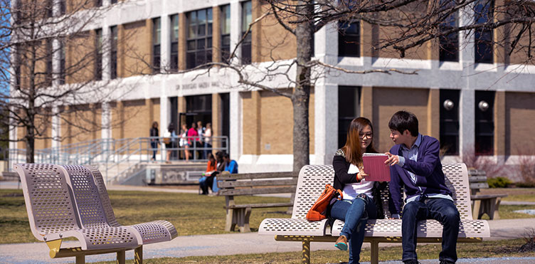 Two students sitting on a bench looking at an iPad